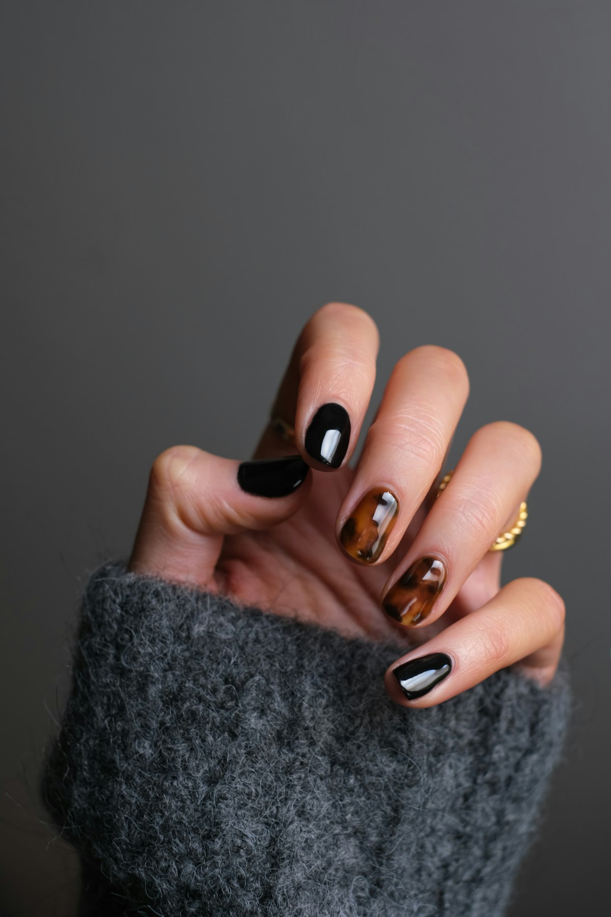 Hand wearing a glossy black and tortoiseshell manicure with a gold ring, holding black fabric