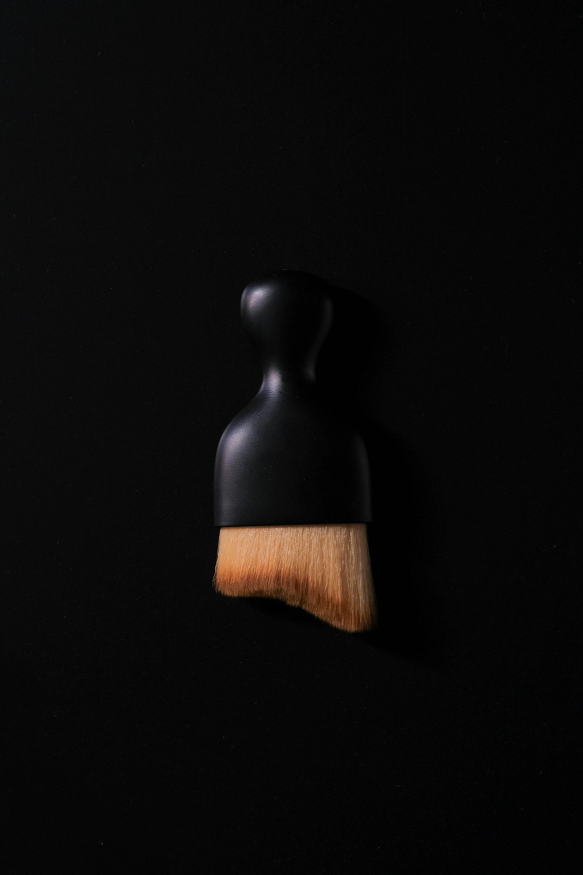 Curved soft-bristle brush with a matte black handle photographed on a black background