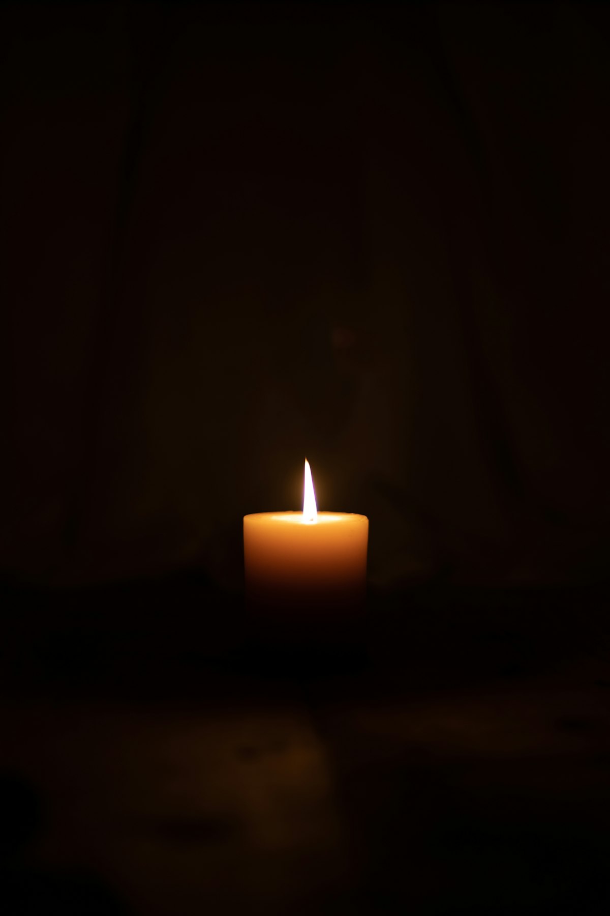 Single lit pillar candle glowing warm amber in a dark room